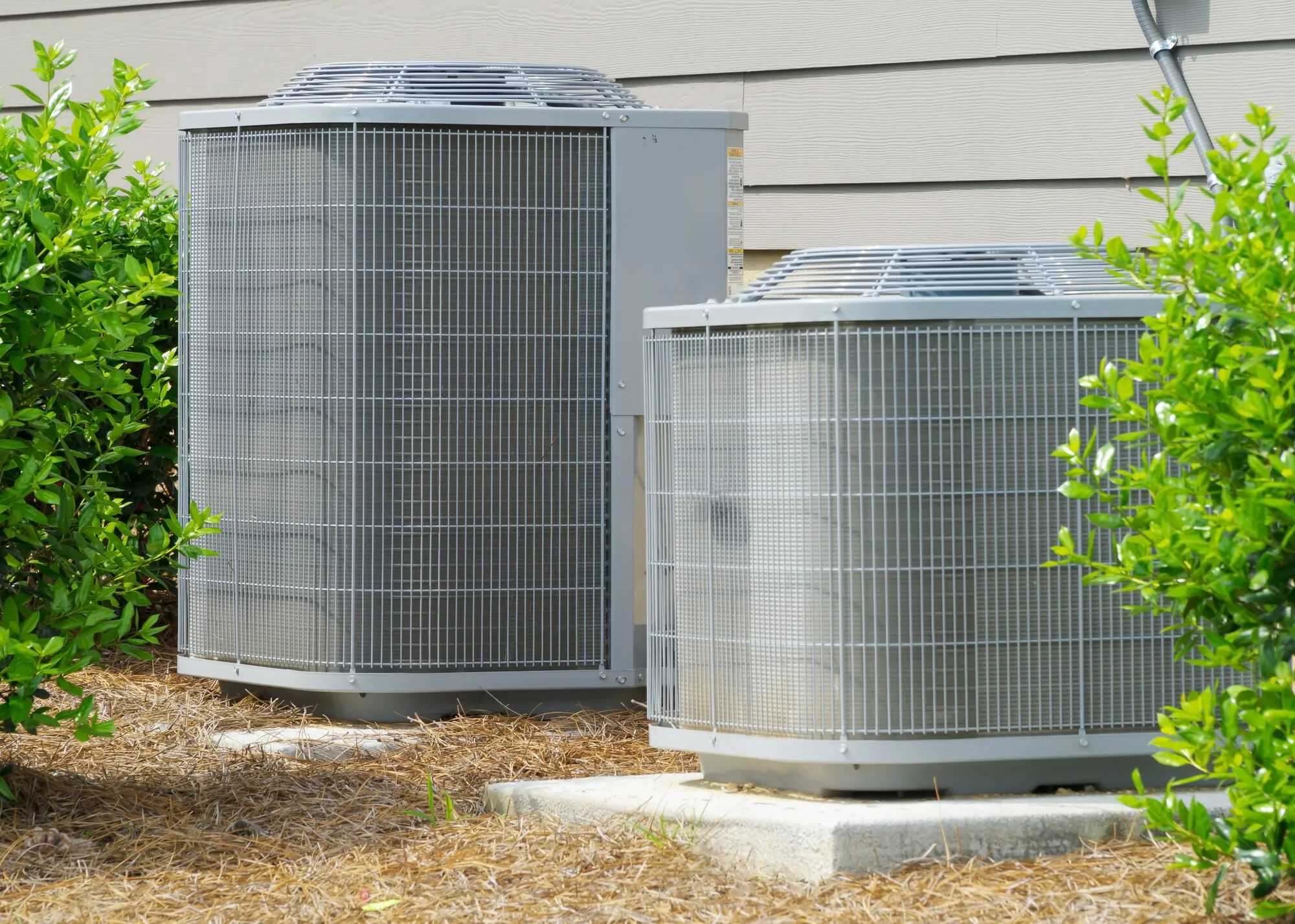 Two residential AC condenser units installed beside a home
